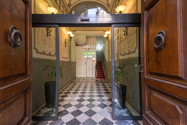 A hotel entrance with a checkered floor, wooden doors, and a staircase leading to the upper level. - Hotel De Lanzi (Florence)