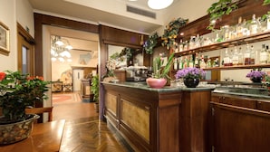 Zona de bar con armarios de madera, encimera de mármol y diversas botellas y plantas.