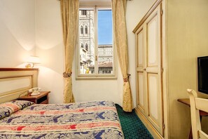 A hotel room with a bed, a nightstand with a telephone, a window with curtains, and a view of a historic building. - Hotel De Lanzi (Florence)