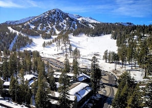 A mountain with a ski slope, surrounded by snow-covered trees and buildings.