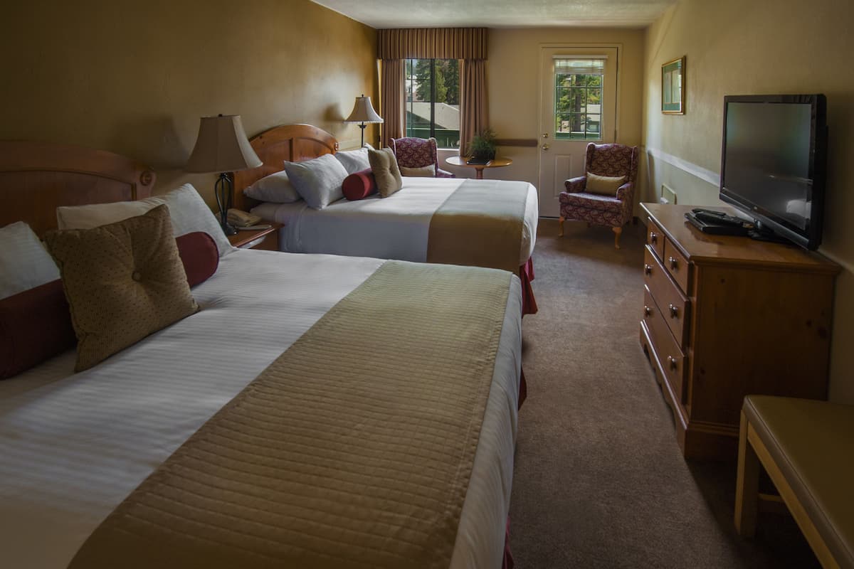 A hotel room with two beds, a television, a desk, and a chair.