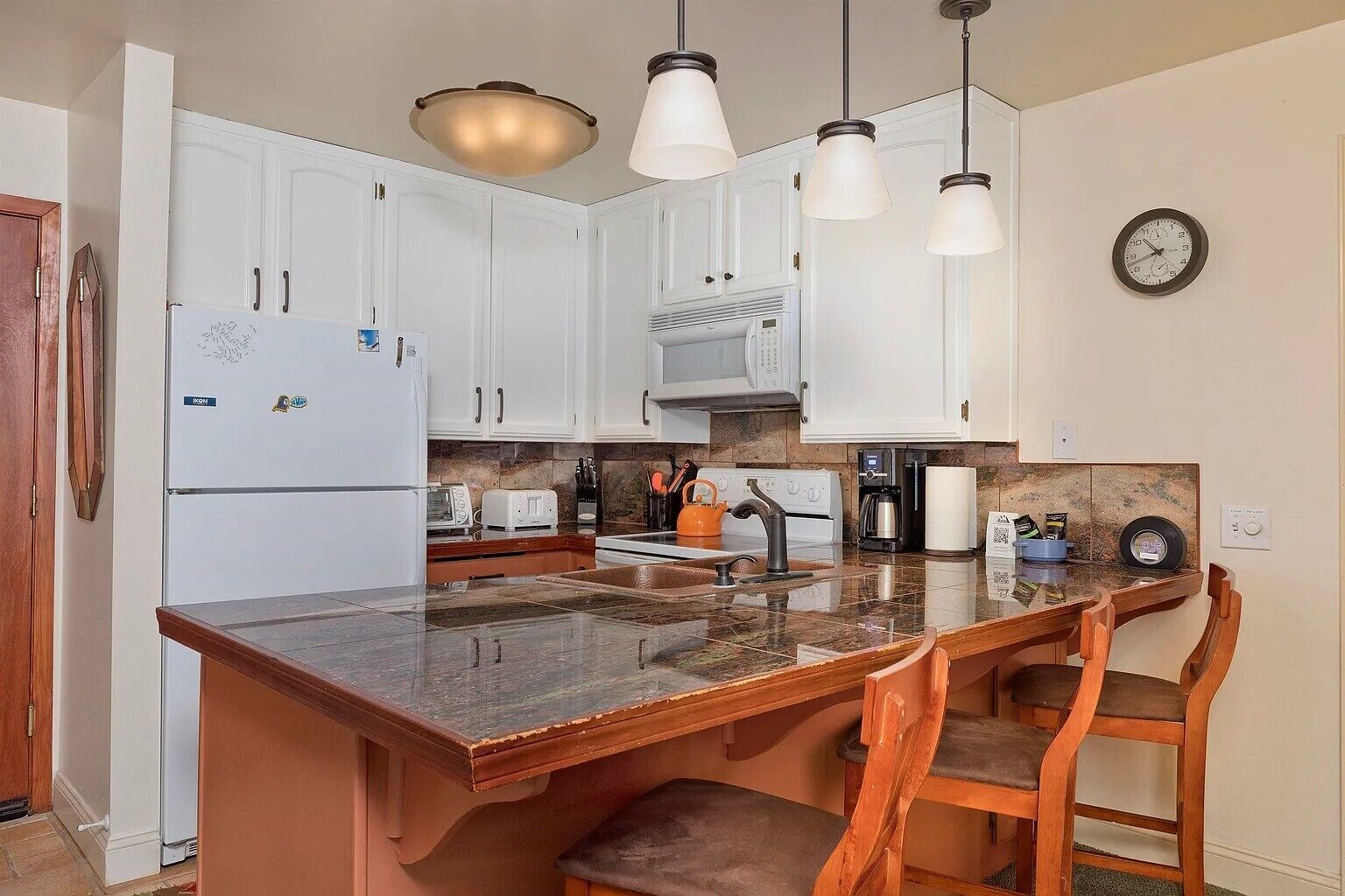 A kitchen with white cabinets, a granite countertop, a stove, a coffee maker, and a clock on the wall.