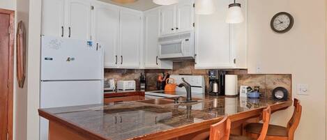 A kitchen with white cabinets, a granite countertop, a stove, a coffee maker, and a clock on the wall.