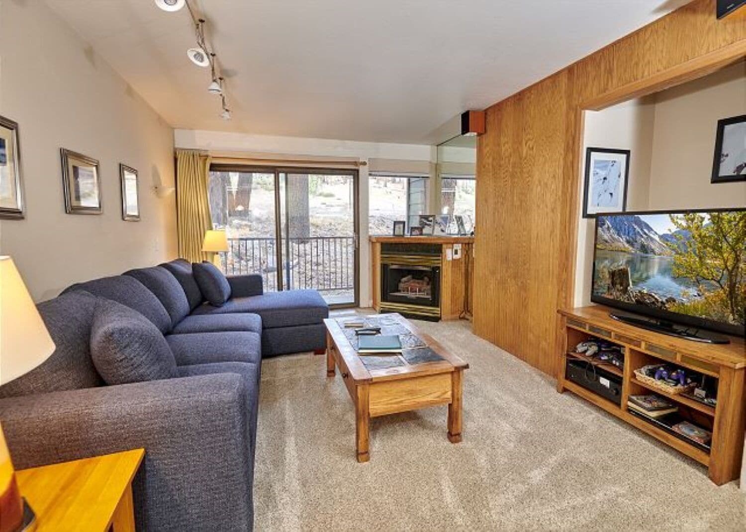 A living room with a sofa, a coffee table, a fireplace, a television, and a balcony with a view.