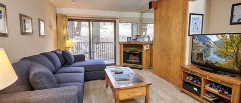A living room with a sofa, a coffee table, a fireplace, a television, and a balcony with a view.