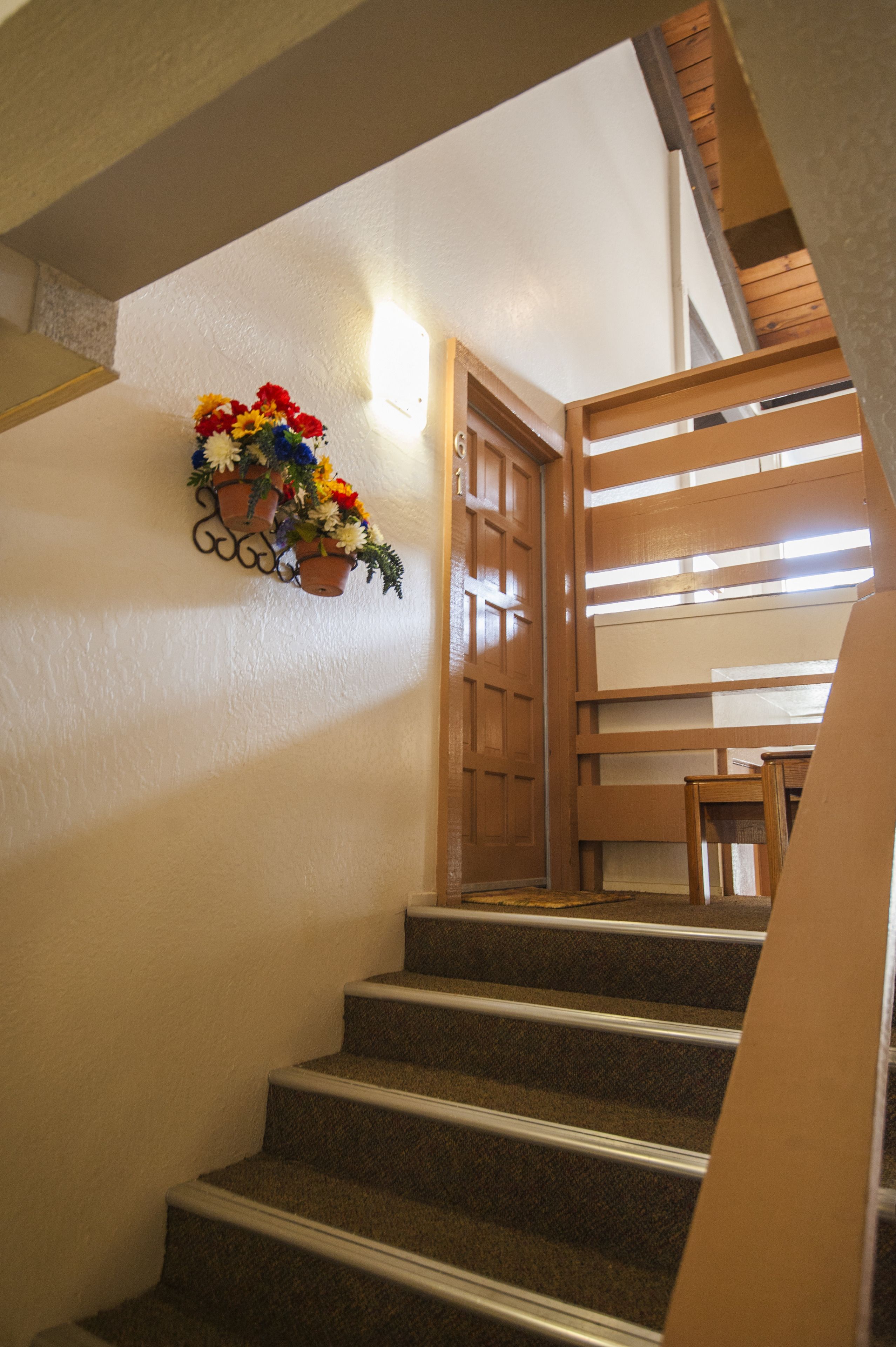 A staircase with carpeted steps, a wooden door, and a wall-mounted flower arrangement.