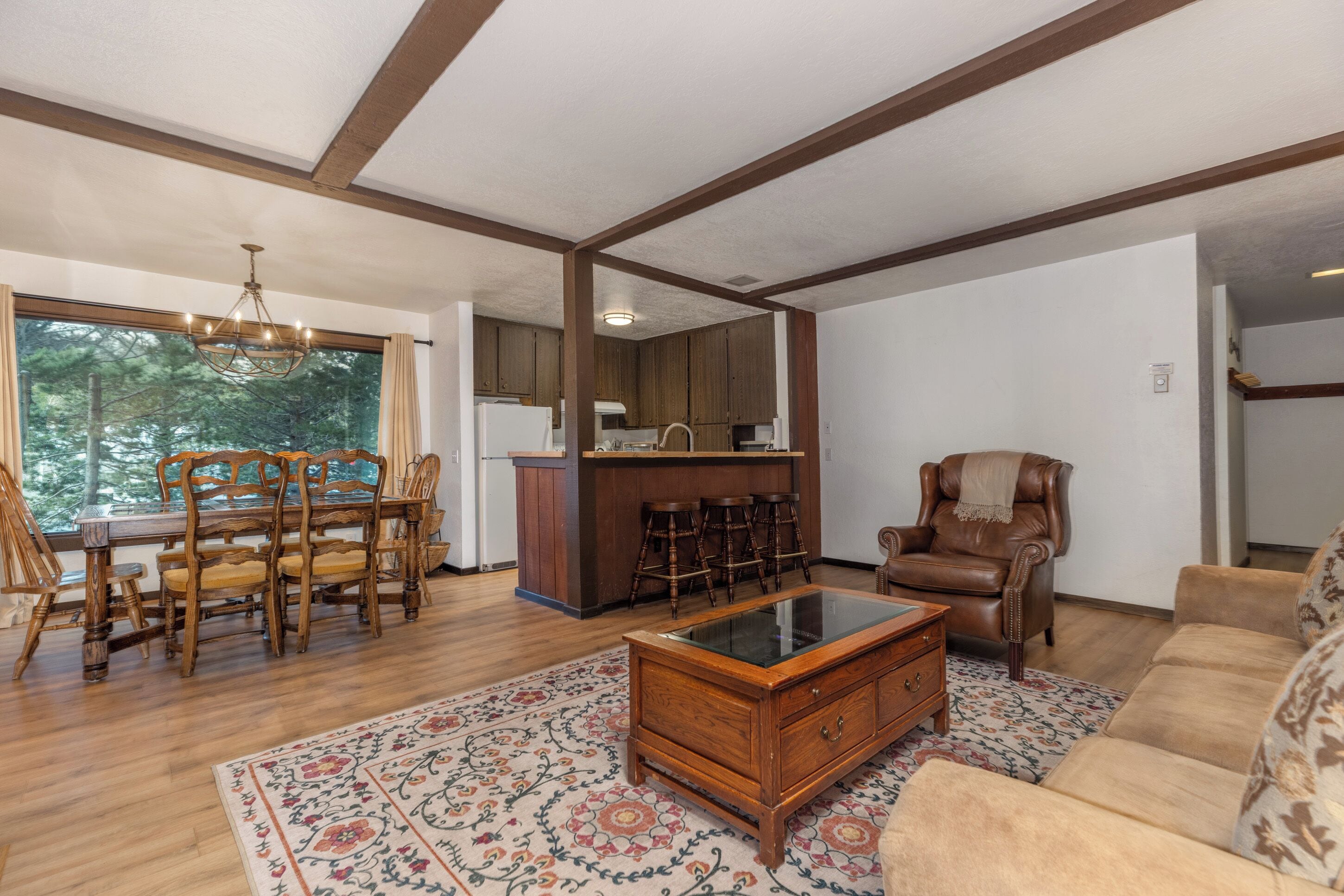 A spacious living room with wooden flooring, a glass coffee table, a leather armchair, and a dining area with wooden chairs and a table.