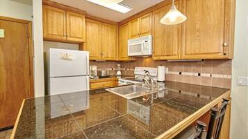 A kitchen with wooden cabinets, a stainless steel sink, a refrigerator, a microwave, and granite countertops.