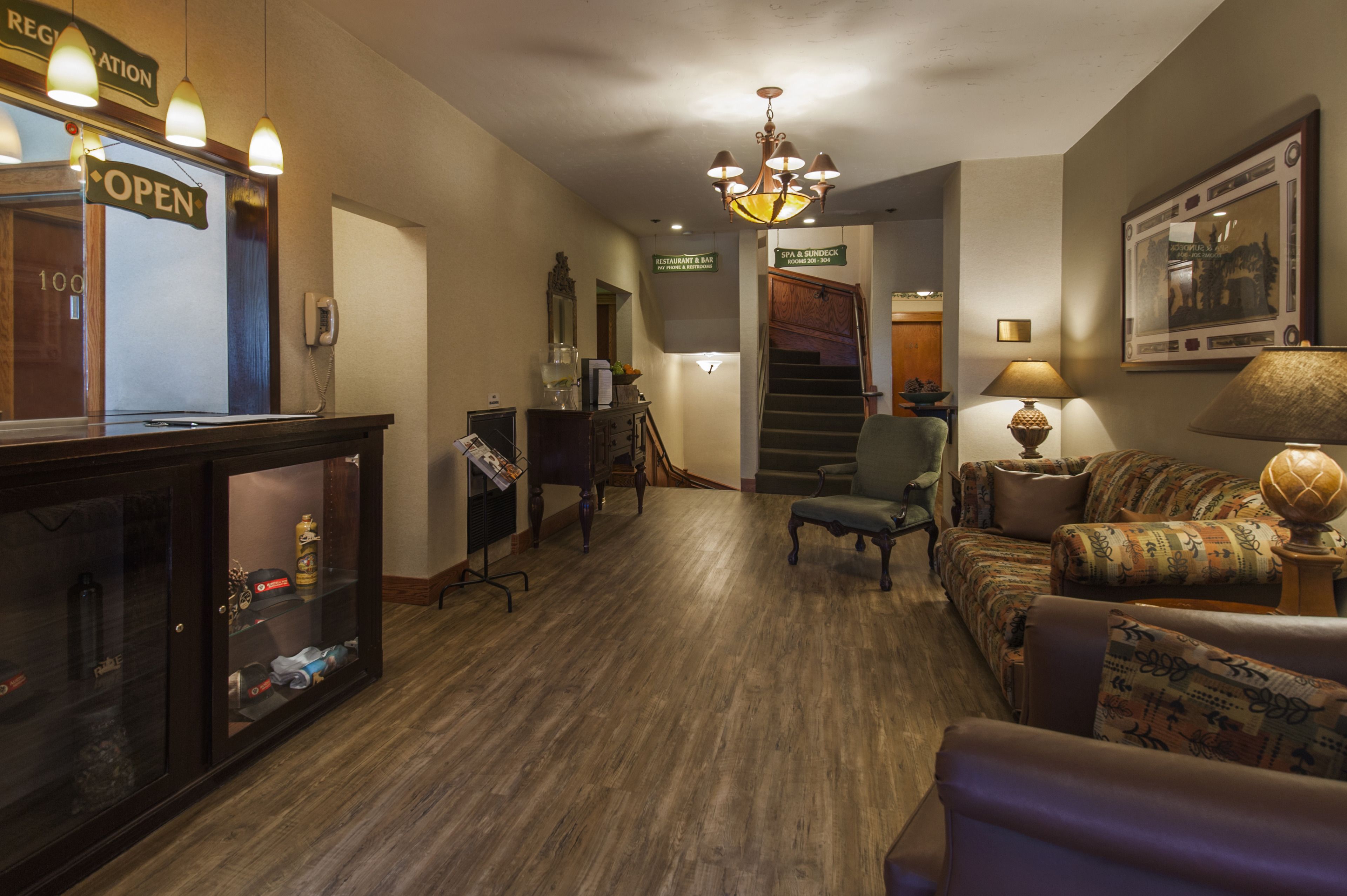 Un vestíbulo de hotel con mostrador de recepción, escalera, sofá y lámpara.