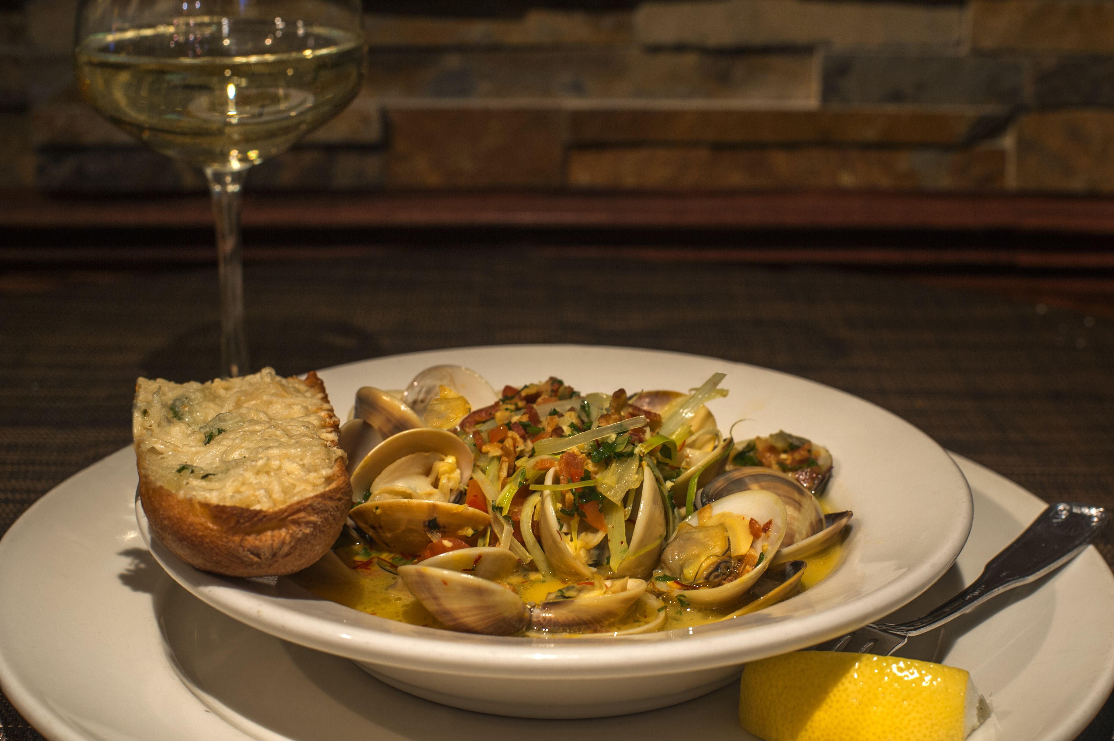 A plate of seafood with bread and a lemon wedge, accompanied by a glass of white wine.