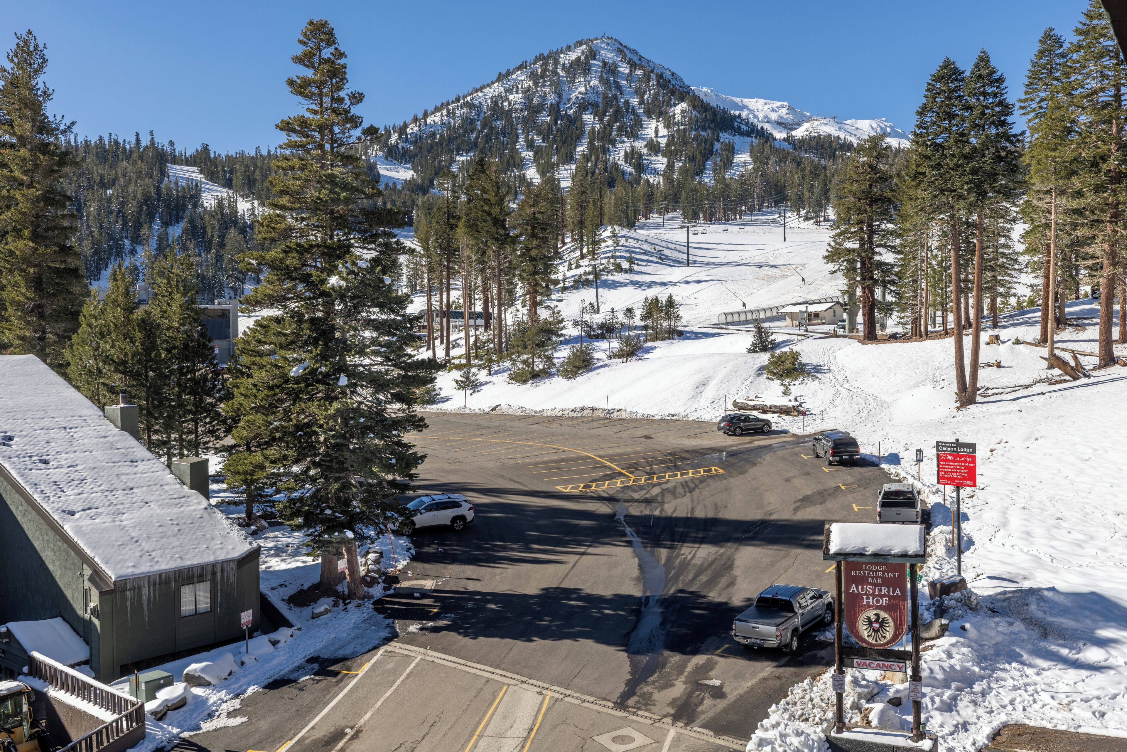 A parking lot with snow-covered ground, a mountain in the background, and a sign for 'Lodge Austria Hof.'