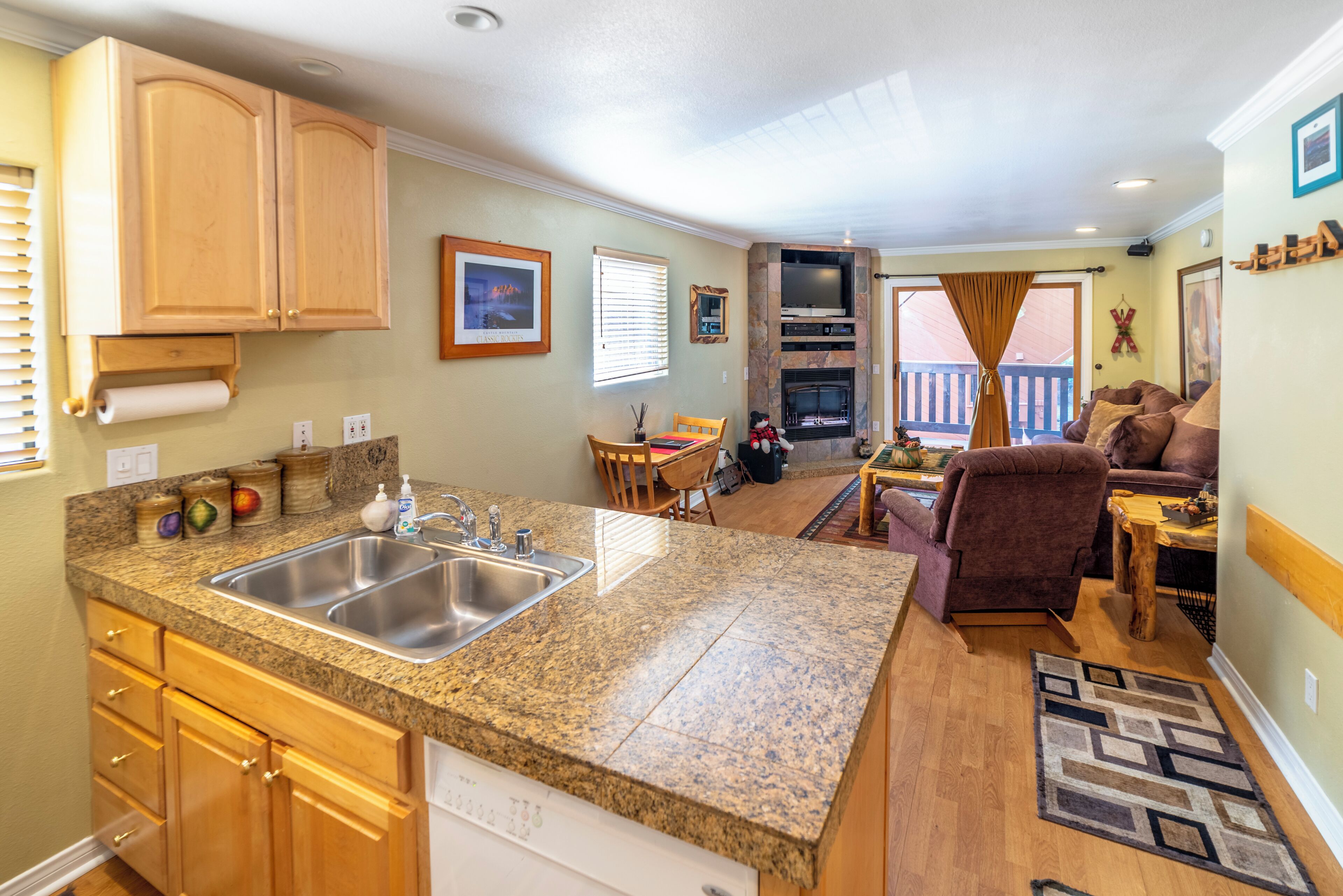 A compact kitchen with granite countertops, wooden cabinets, and a built-in dishwasher.