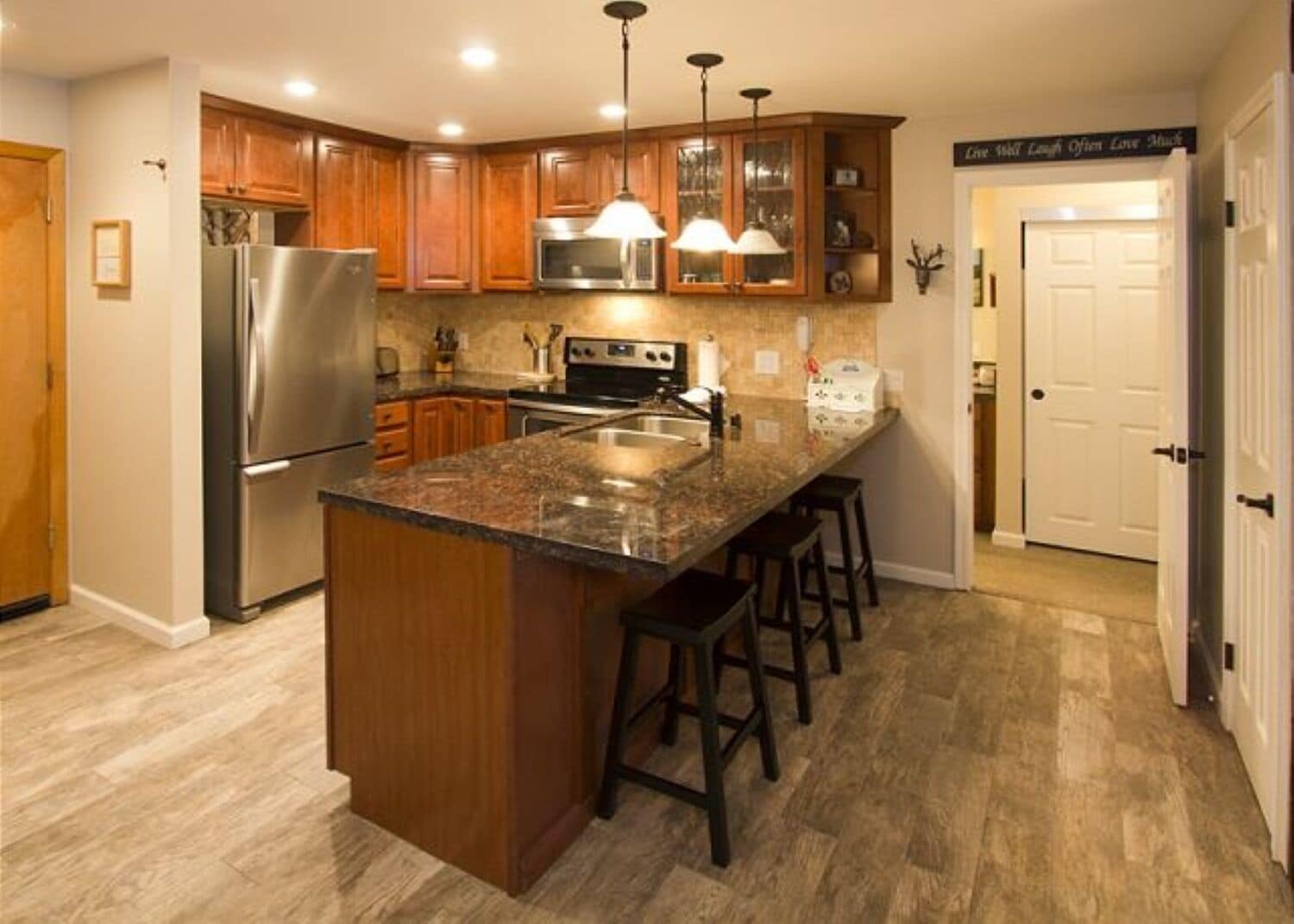 A kitchen with wooden cabinets, a stainless steel refrigerator, a granite countertop, and pendant lighting.