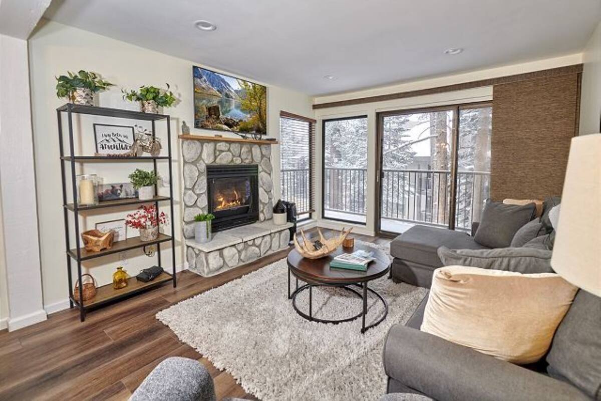 A living room with a stone fireplace, a grey sofa, a coffee table, and a bookshelf.