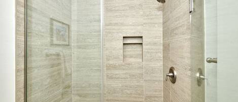 A glass-enclosed shower with a handheld showerhead, a small shelf, and a door with a handle.