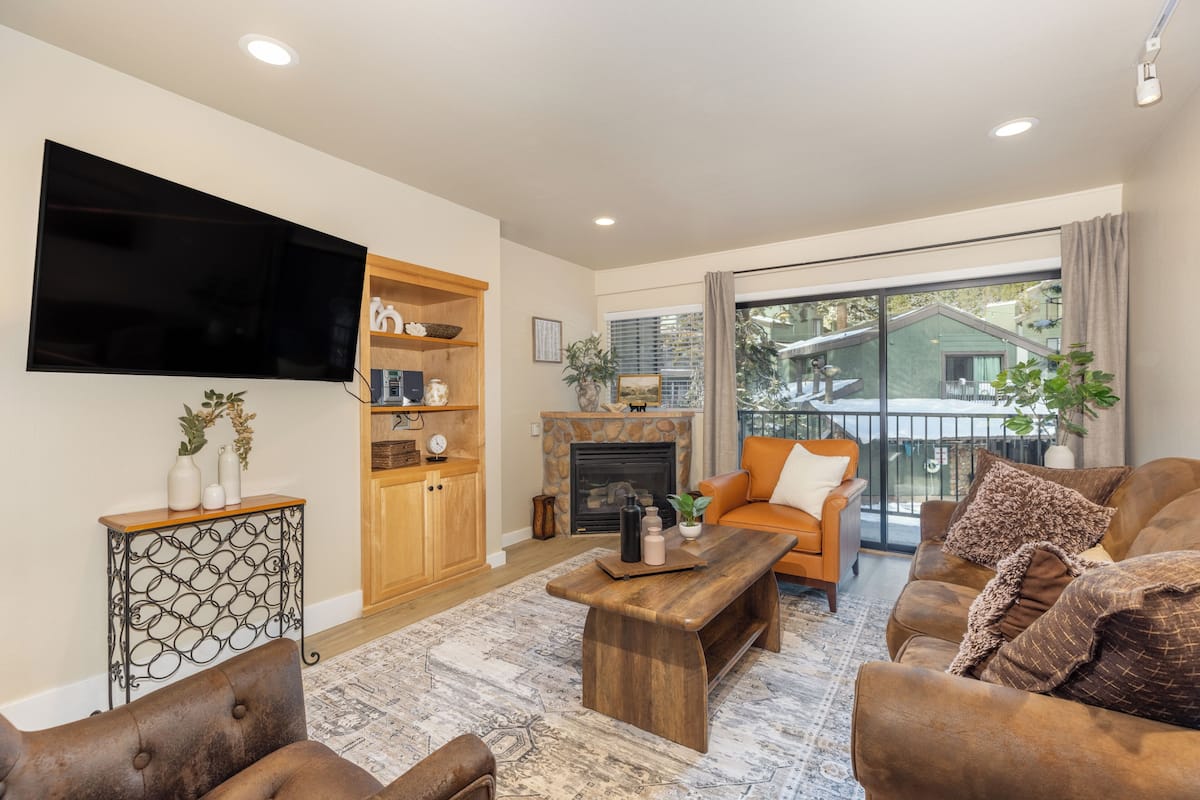 A living room with a flat-screen TV, wooden furniture, a fireplace, and a balcony with a view.