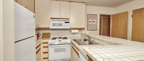 A compact kitchen with a refrigerator, stove, microwave, and sink.