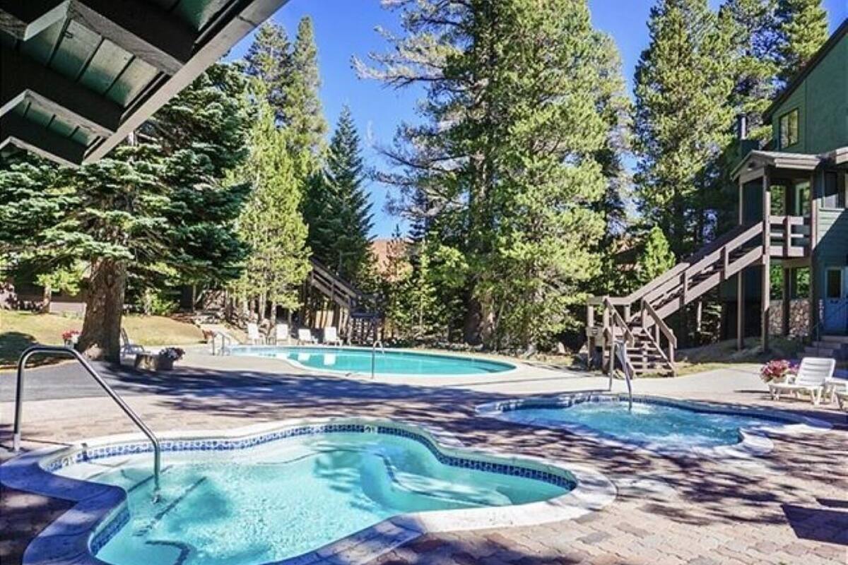 A pool area with two hot tubs, surrounded by trees and a building with a covered deck.