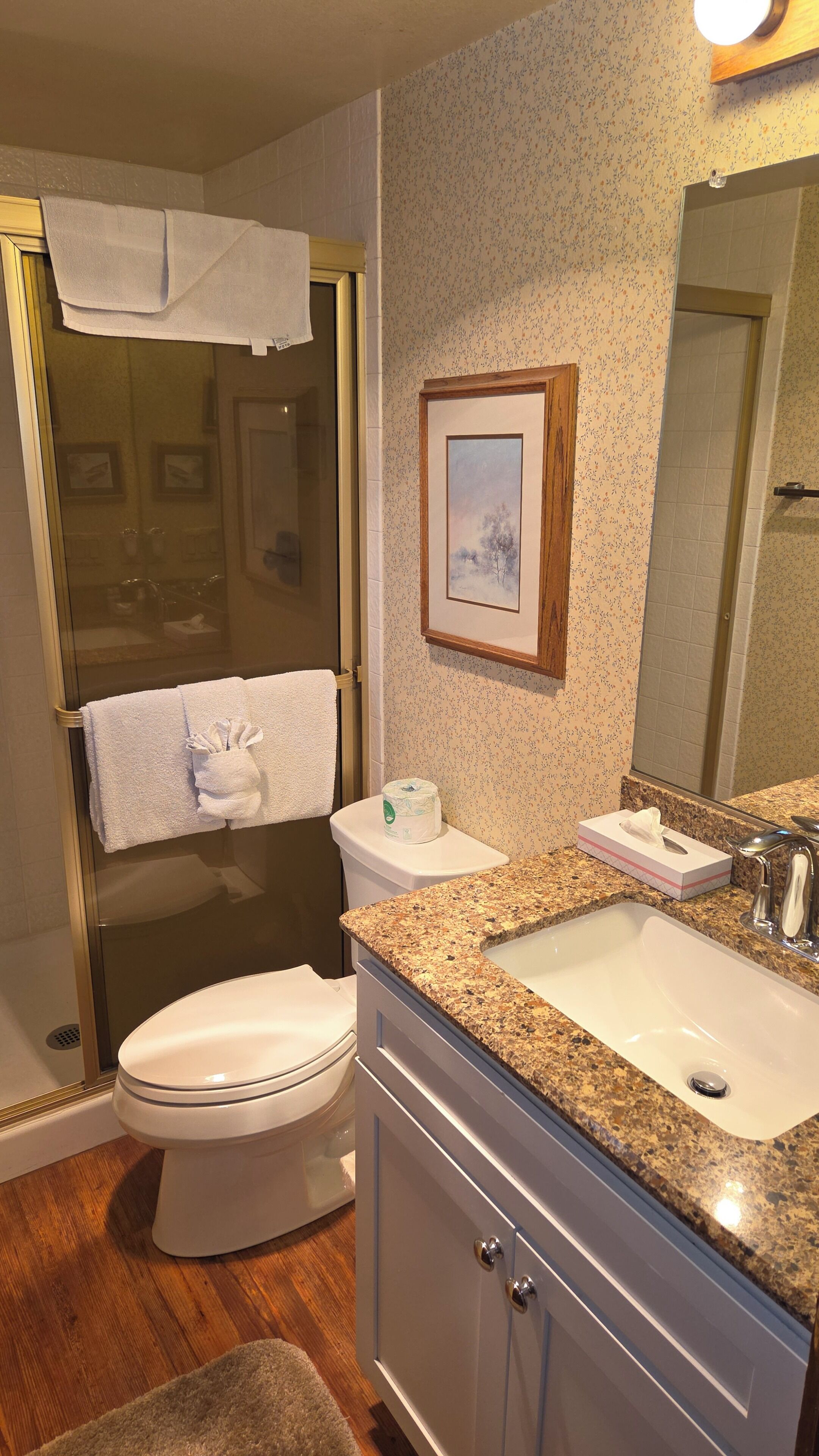A bathroom with a toilet, sink, shower, and a framed picture on the wall.