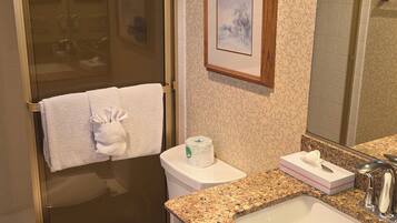 A bathroom with a toilet, sink, shower, and a framed picture on the wall.