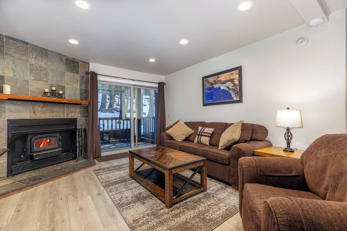 A living room with a fireplace, a sofa, a coffee table, and a view through a glass door.