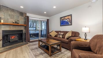 A living room with a fireplace, a sofa, a coffee table, and a view through a glass door.