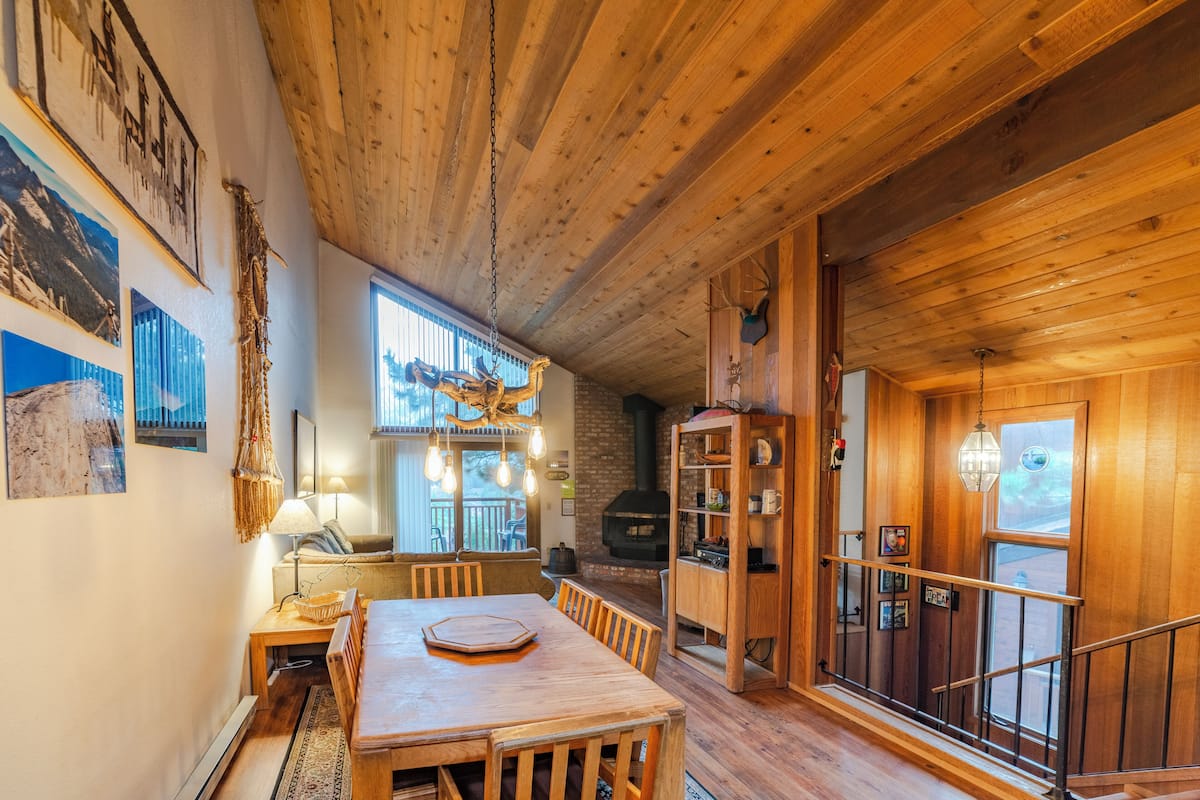A wooden interior with a dining table, chairs, a bookshelf, and a fireplace.