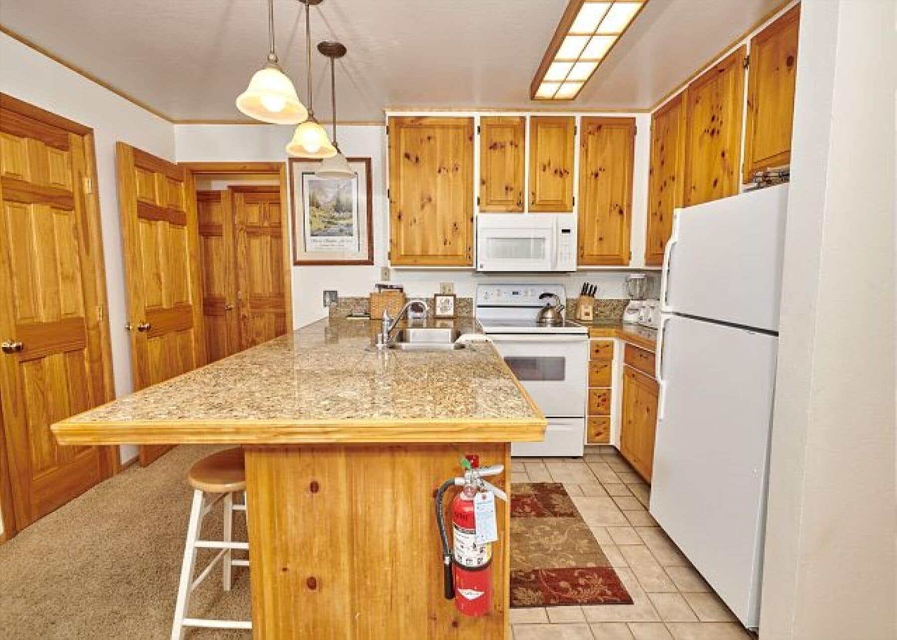 A kitchen with wooden cabinets, a granite countertop, a white refrigerator, a stove, a microwave, and a fire extinguisher.