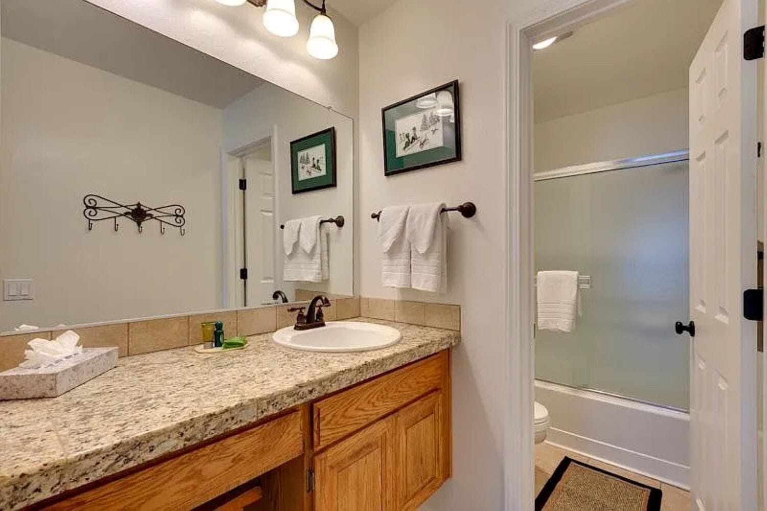 A bathroom with a granite countertop, wooden cabinets, a sink, a mirror, and a shower area.