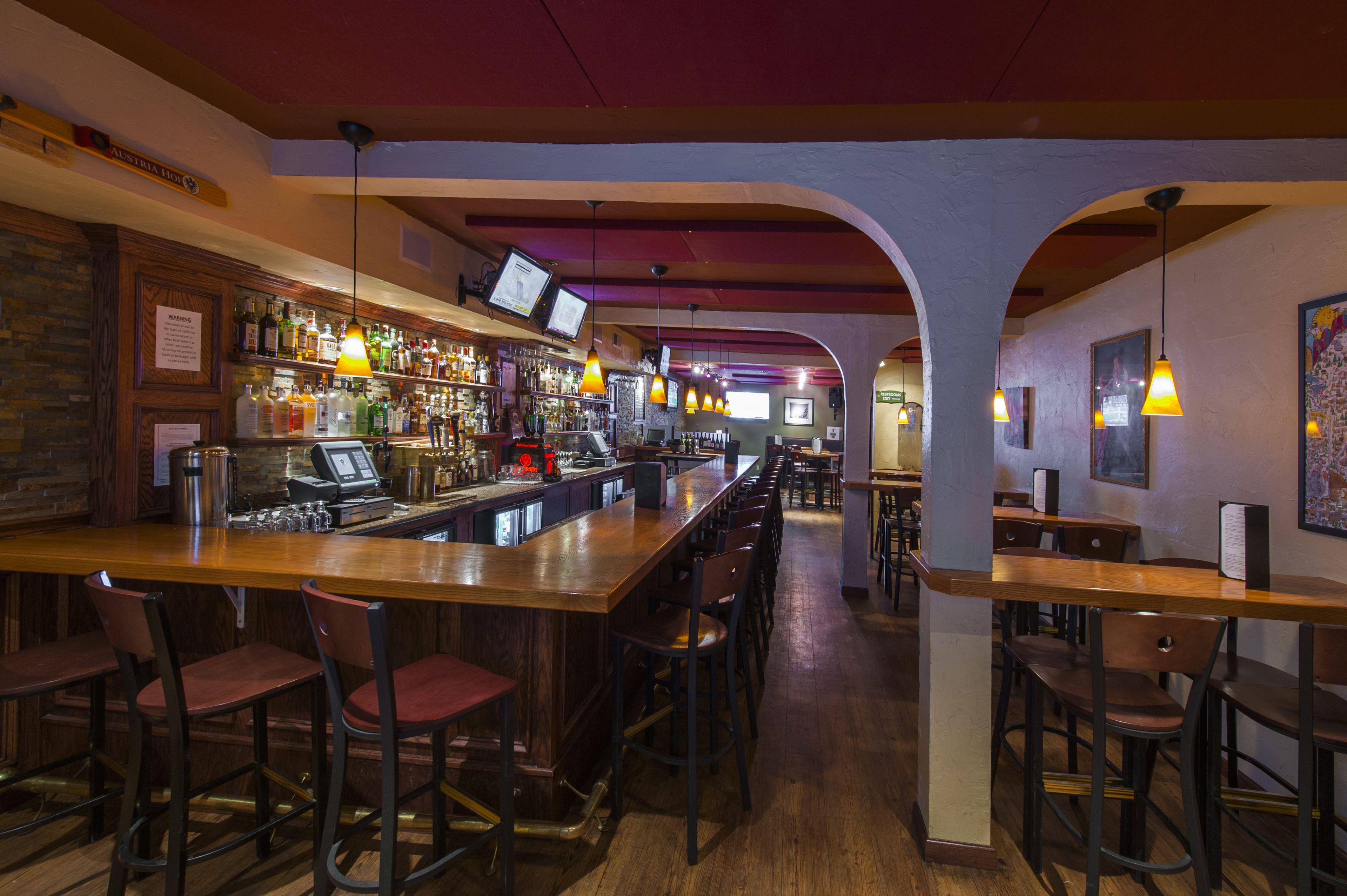 A bar with wooden bar stools, a cash register, and a variety of liquor bottles.