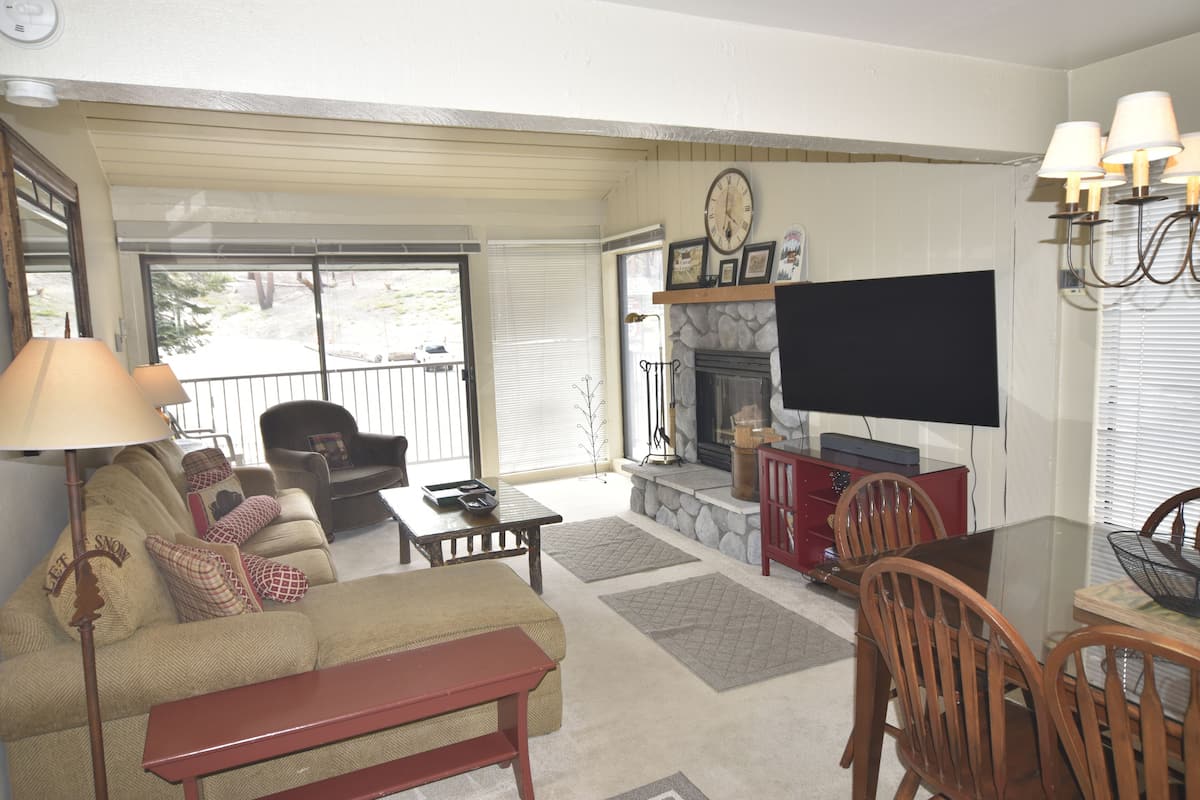 A living room with a sofa, a coffee table, a fireplace, a TV, and a dining area with chairs and a table.