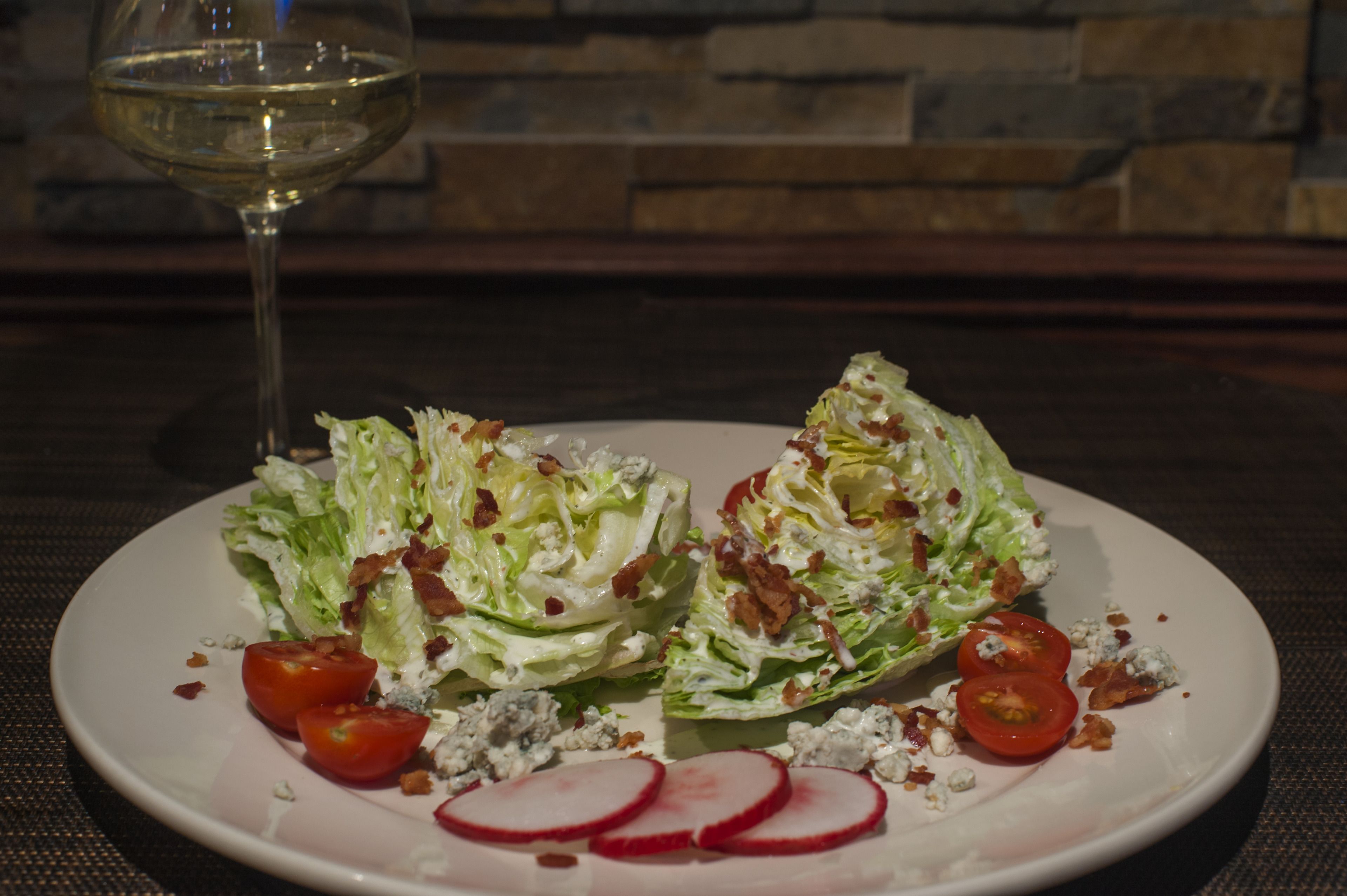 A plate of salad with lettuce, tomatoes, radishes, and crumbled blue cheese, accompanied by a glass of white wine.