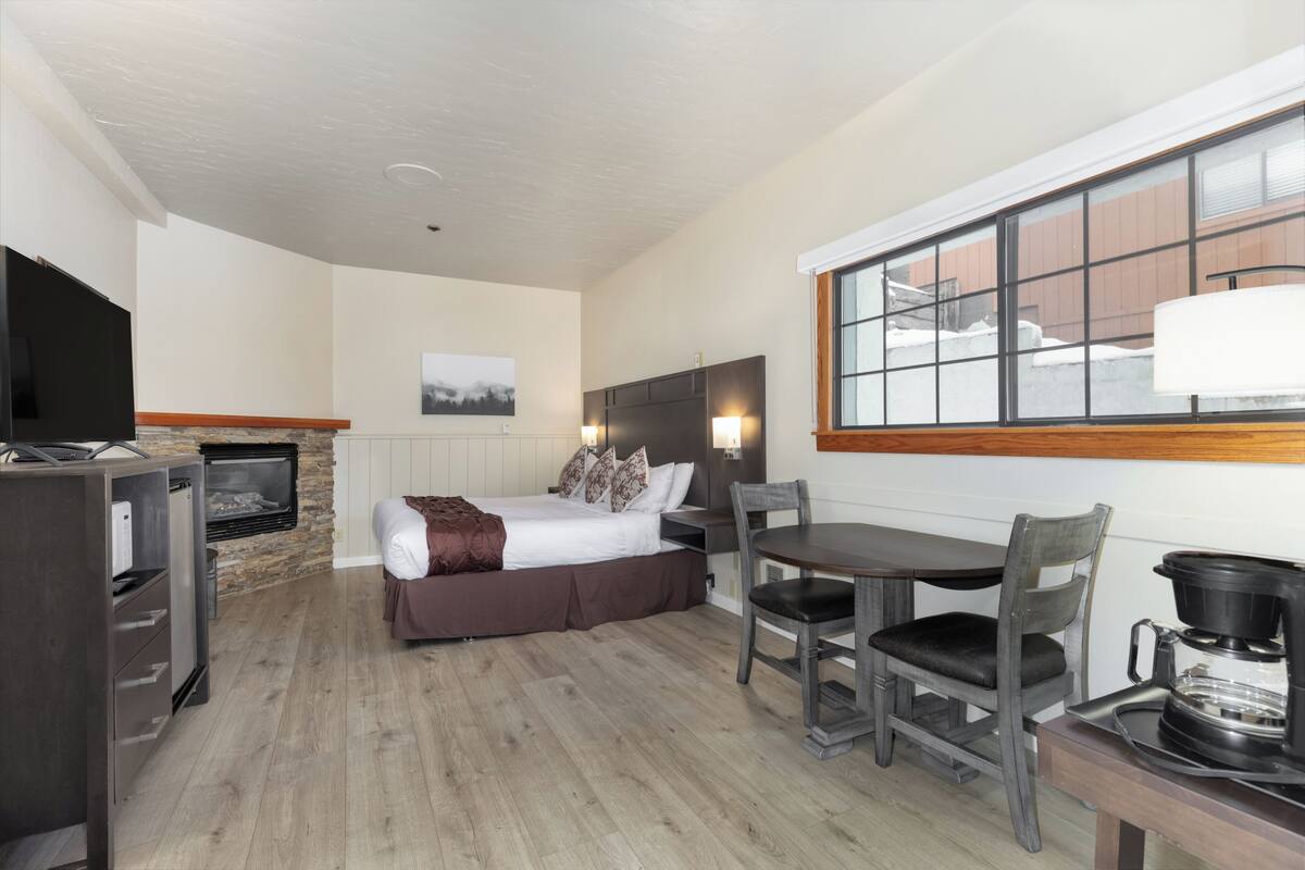 A hotel room with a bed, a desk, a chair, a television, a fireplace, and a window.