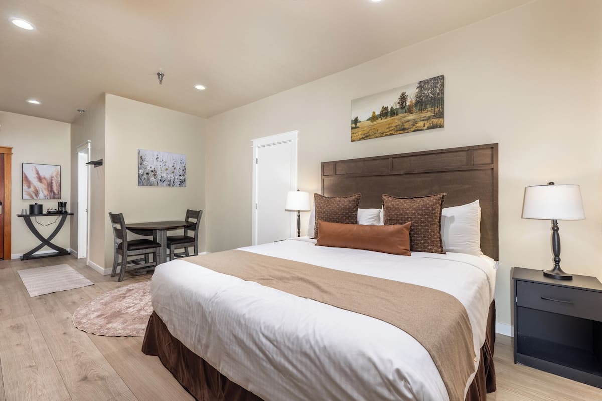 A bedroom with a large bed, a wooden headboard, two bedside lamps, a dining table, and chairs.