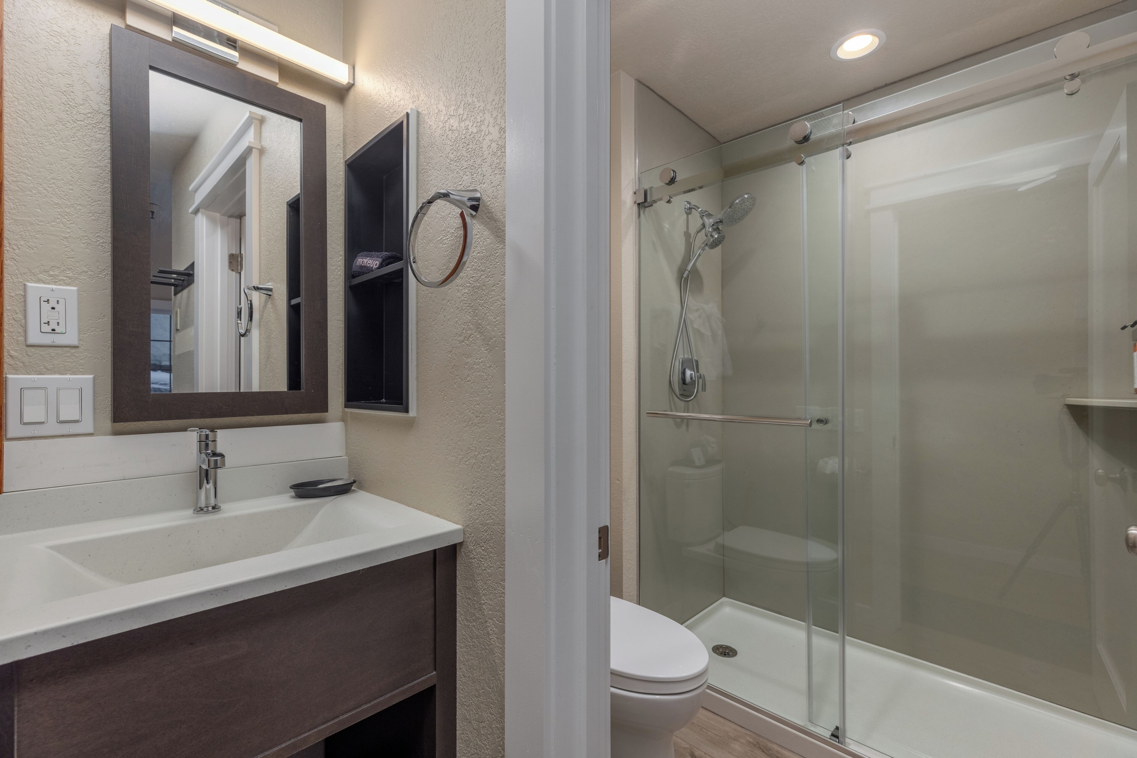 Un baño con lavamanos blanco, espejo, cabina de ducha de vidrio y retrete.