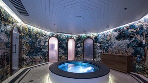 A modern spa area with a central hot tub, mosaic walls, and a wooden cabinet.