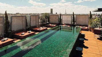 Une piscine sur le toit, avec une eau cristalline, entourée d’espaces de détente comprenant des chaises longues et des plantes en pot.