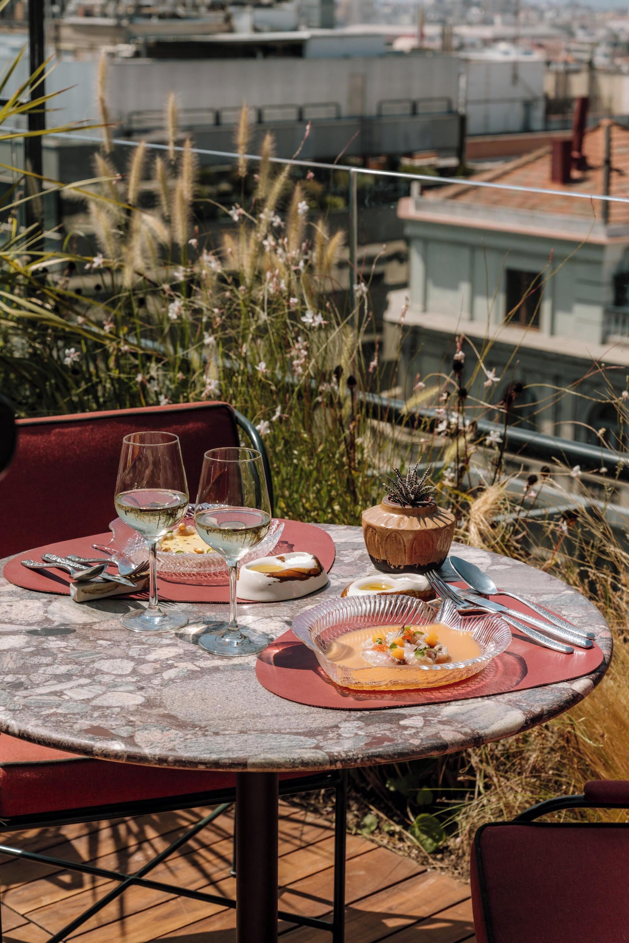 A table set for a meal with wine glasses, plates, and cutlery, overlooking a cityscape.
