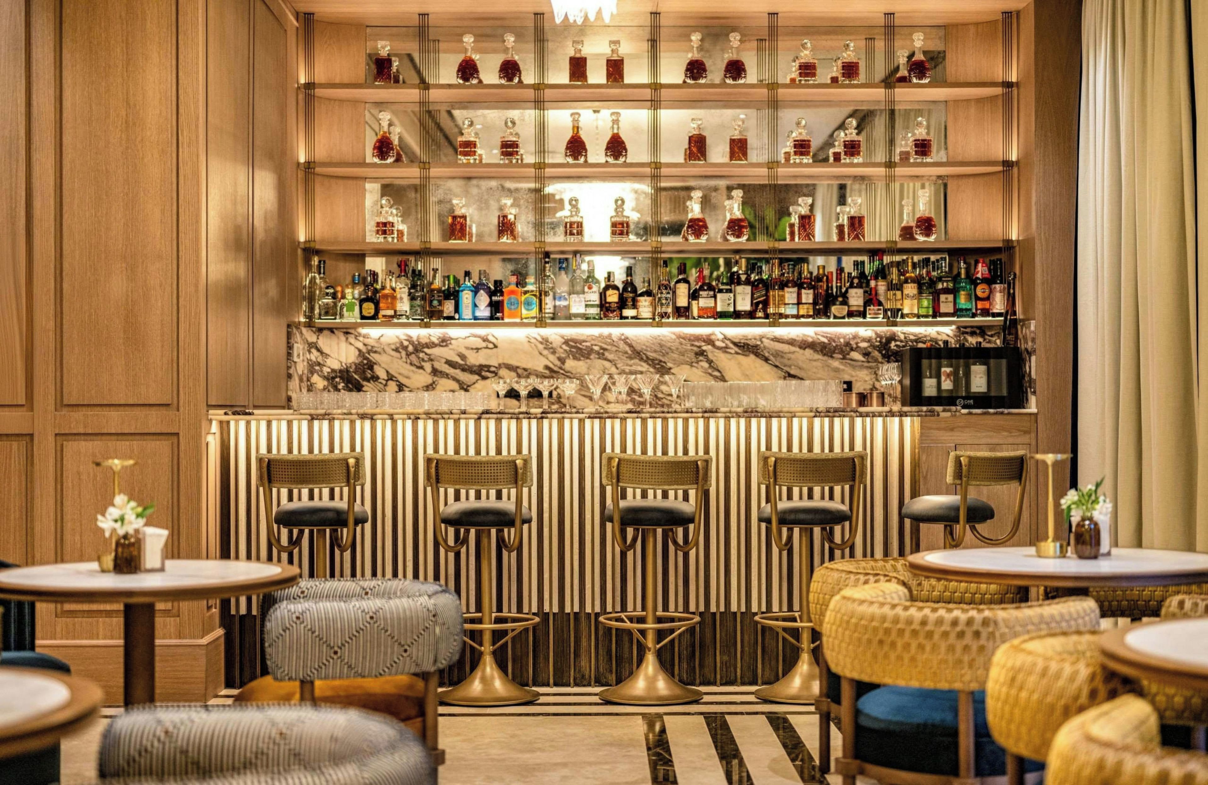 Zona de bar con diversas opciones de asientos, una barra de mármol y una variedad de botellas de licor.