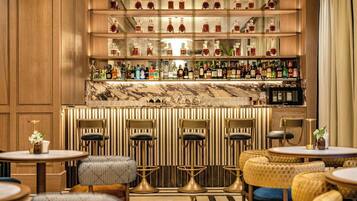 Zona de bar con diversas opciones de asientos, una barra de mármol y una variedad de botellas de licor.