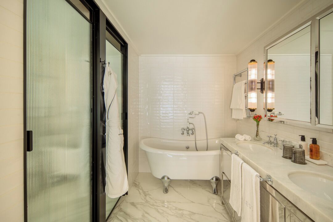 A modern bathroom with a freestanding bathtub, a double sink vanity, and a large mirror with wall sconces.