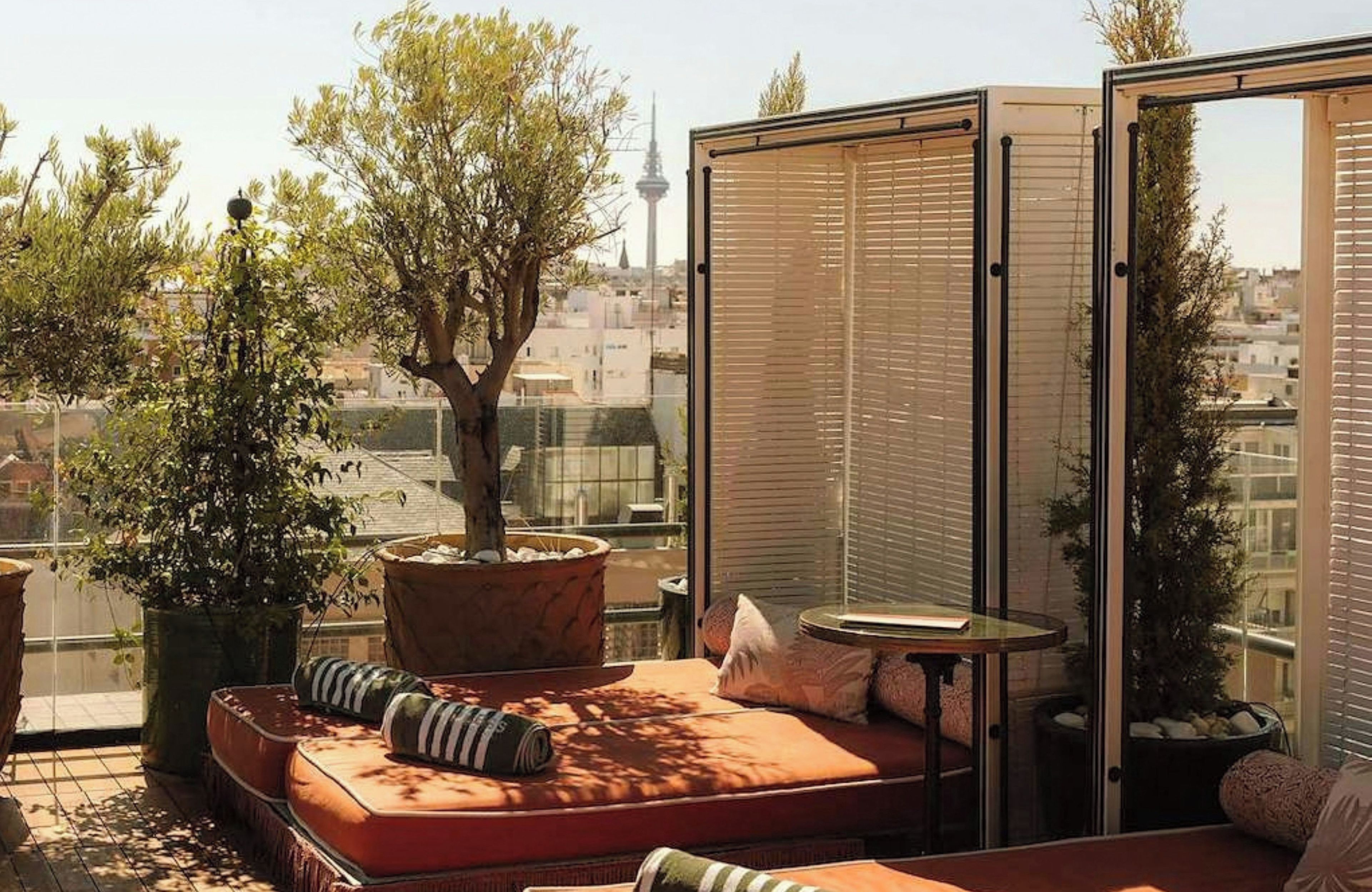 Een balkon met een bank, een potplant en uitzicht op een stadsgezicht, inclusief een toren.