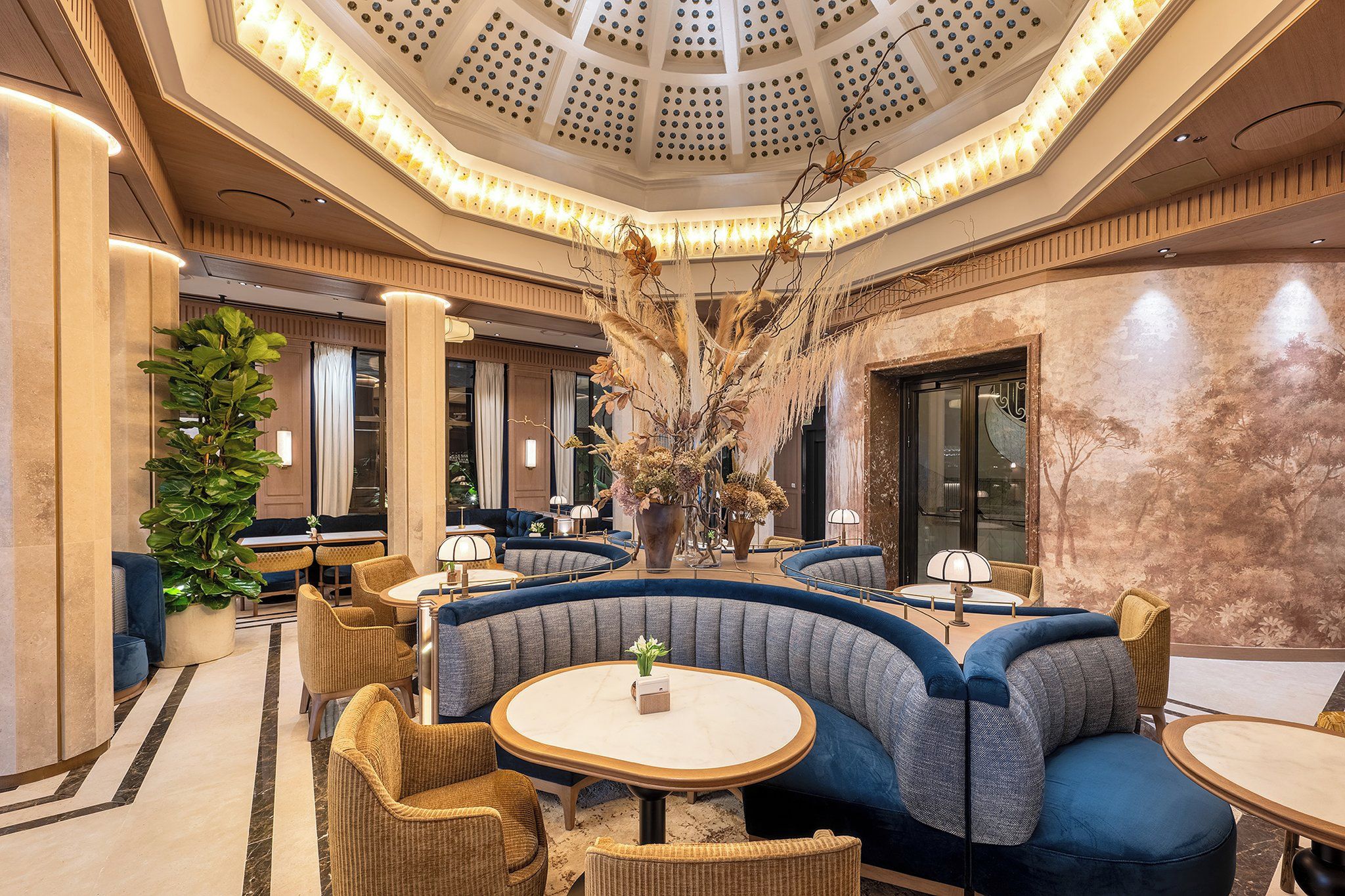 A modern hotel lobby with a central seating area, large windows, and a decorative ceiling.