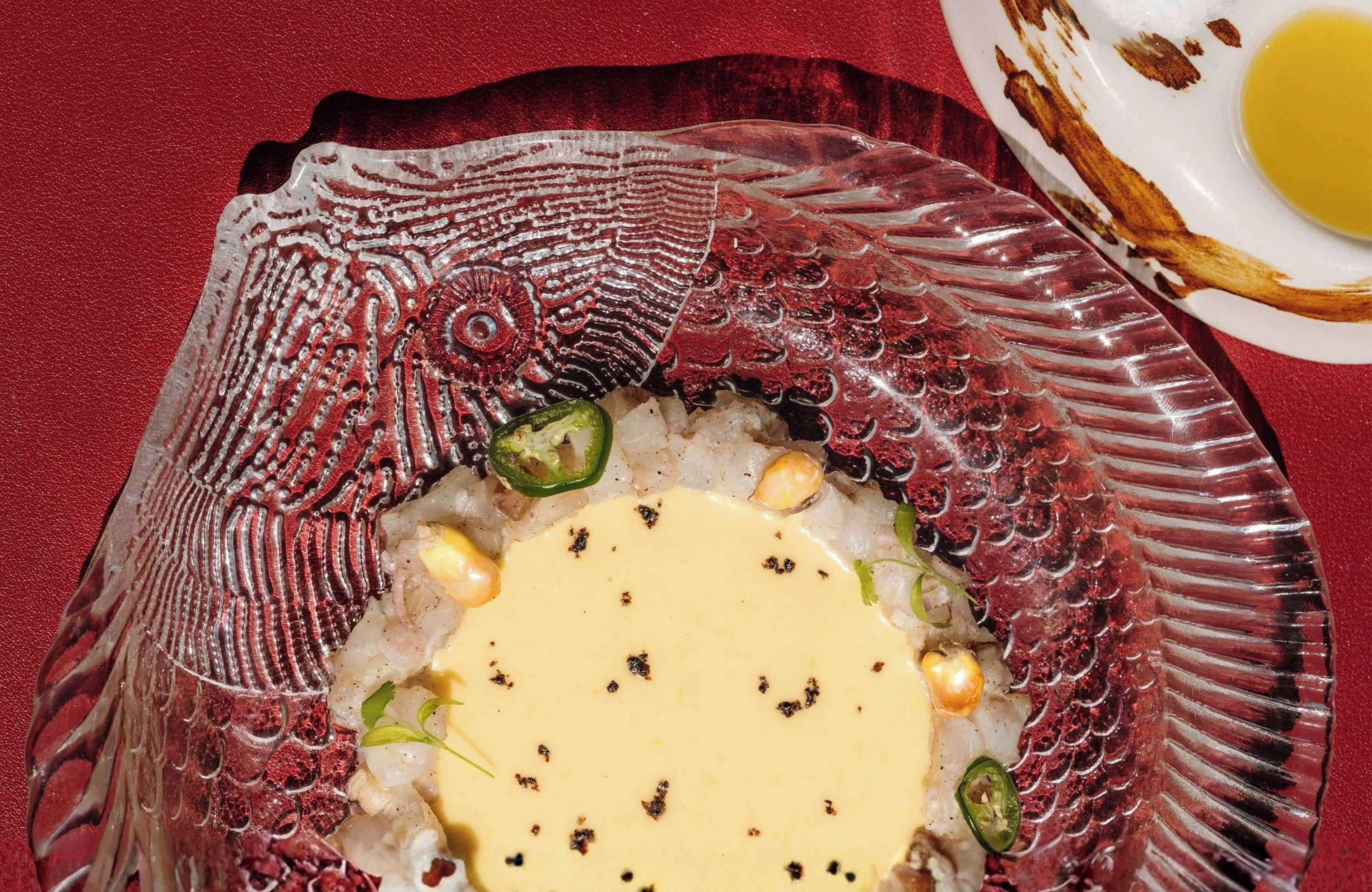 A plate with a fish dish, garnished with herbs and spices, on a red textured tablecloth.