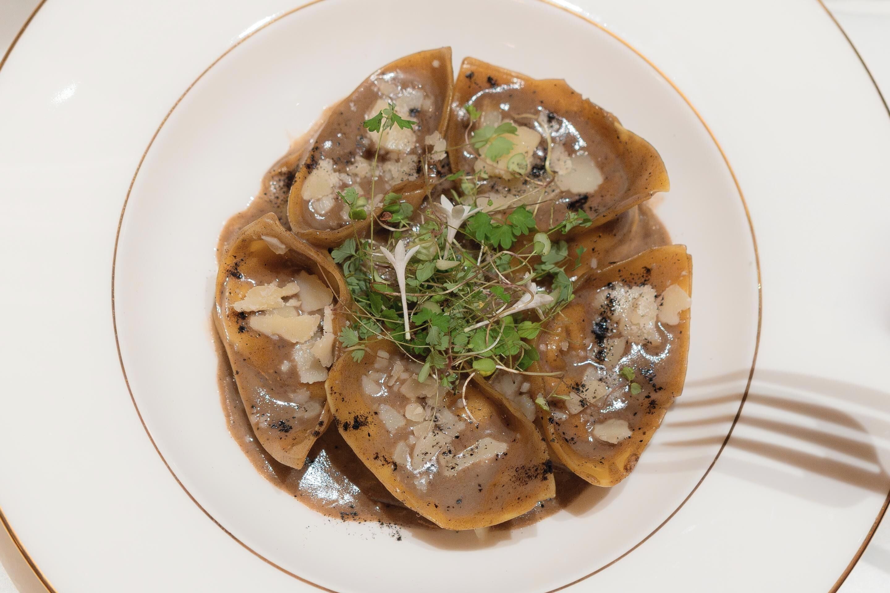 A plate of ravioli with a creamy sauce and garnished with herbs.