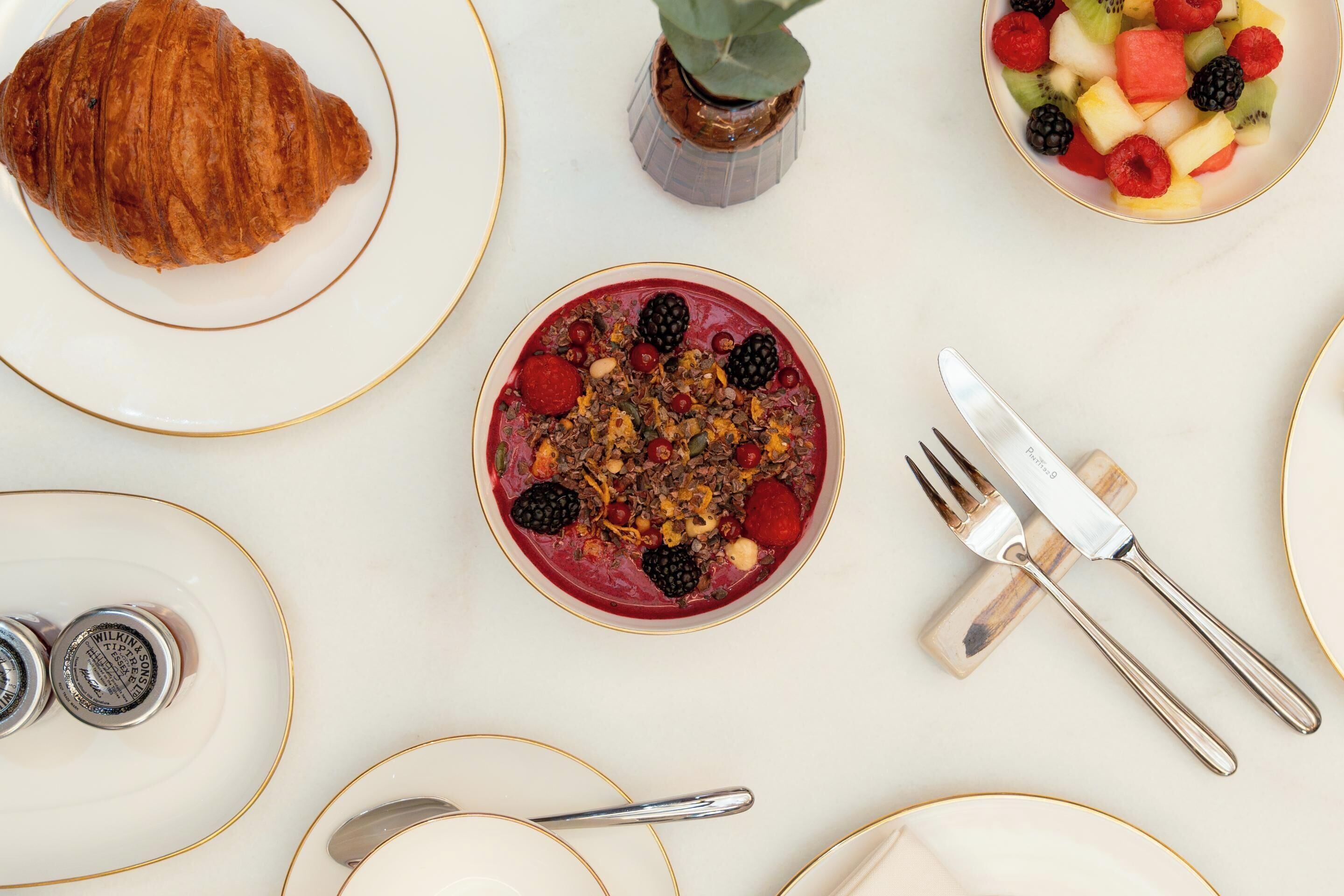 Un desayuno con un croissant, una ensalada de frutas y un tazón de bayas y granola.