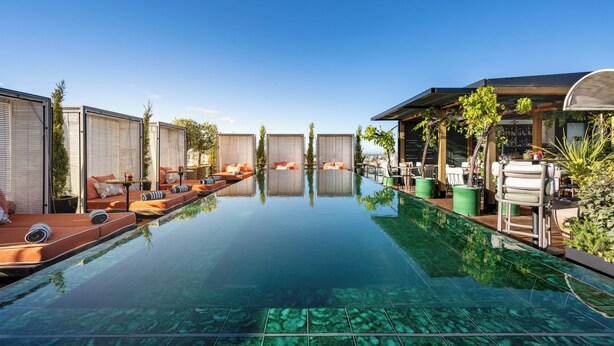 A clear pool with lounge areas on both sides, a covered seating area, and a view of the sky.