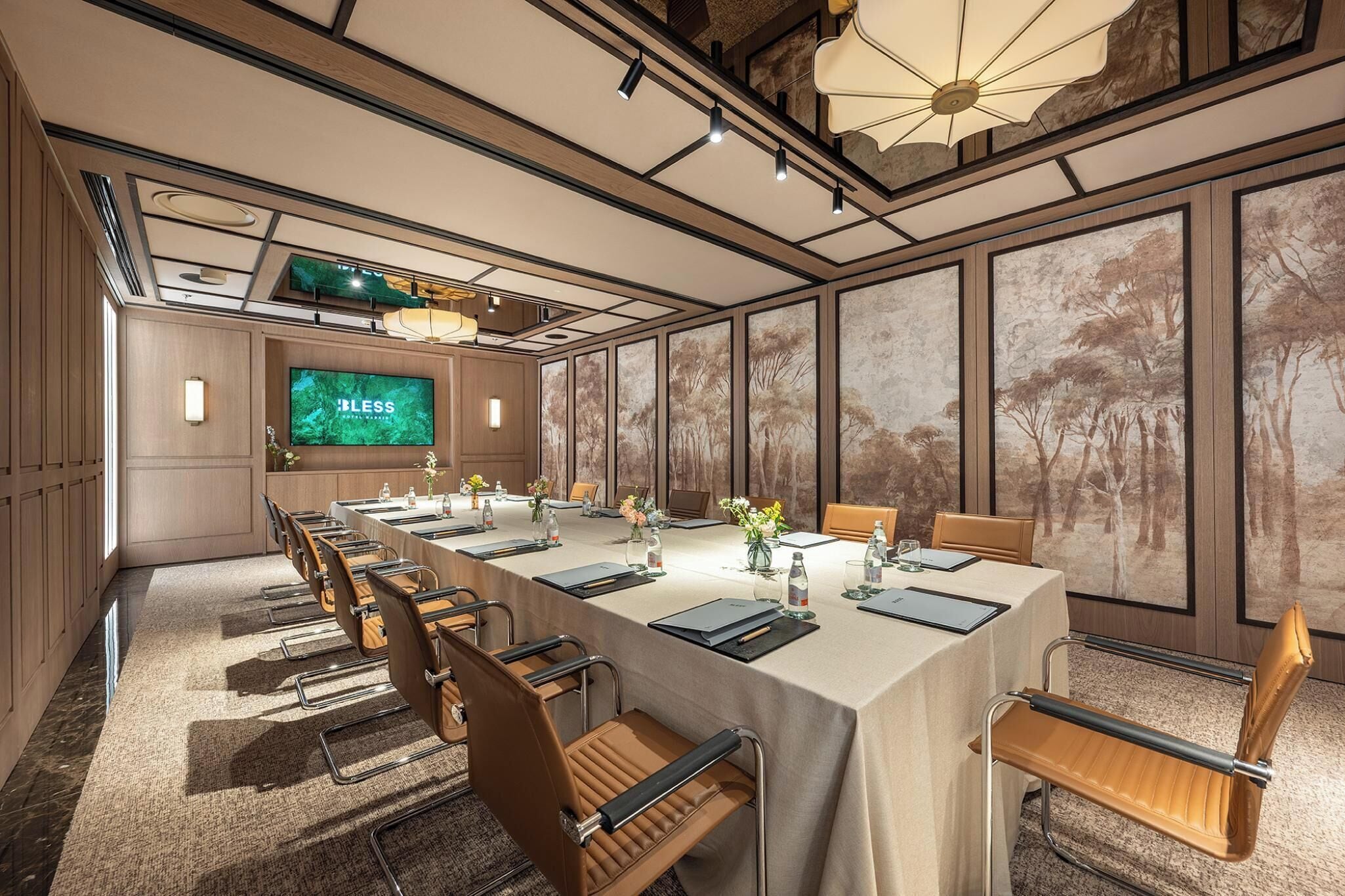 A conference room with a long table, chairs, a large screen, and a forest mural.