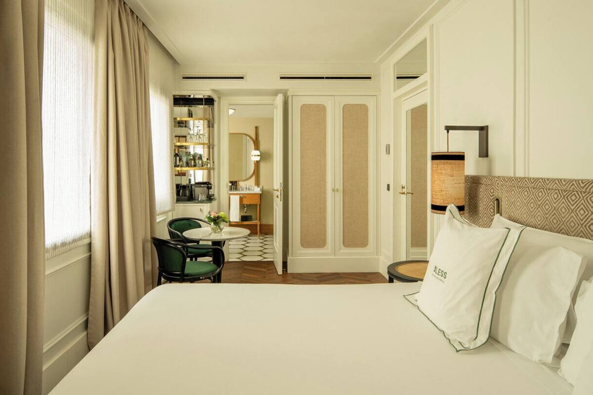 A hotel room with a bed, a desk, a chair, a small table with a vase, and a wardrobe.