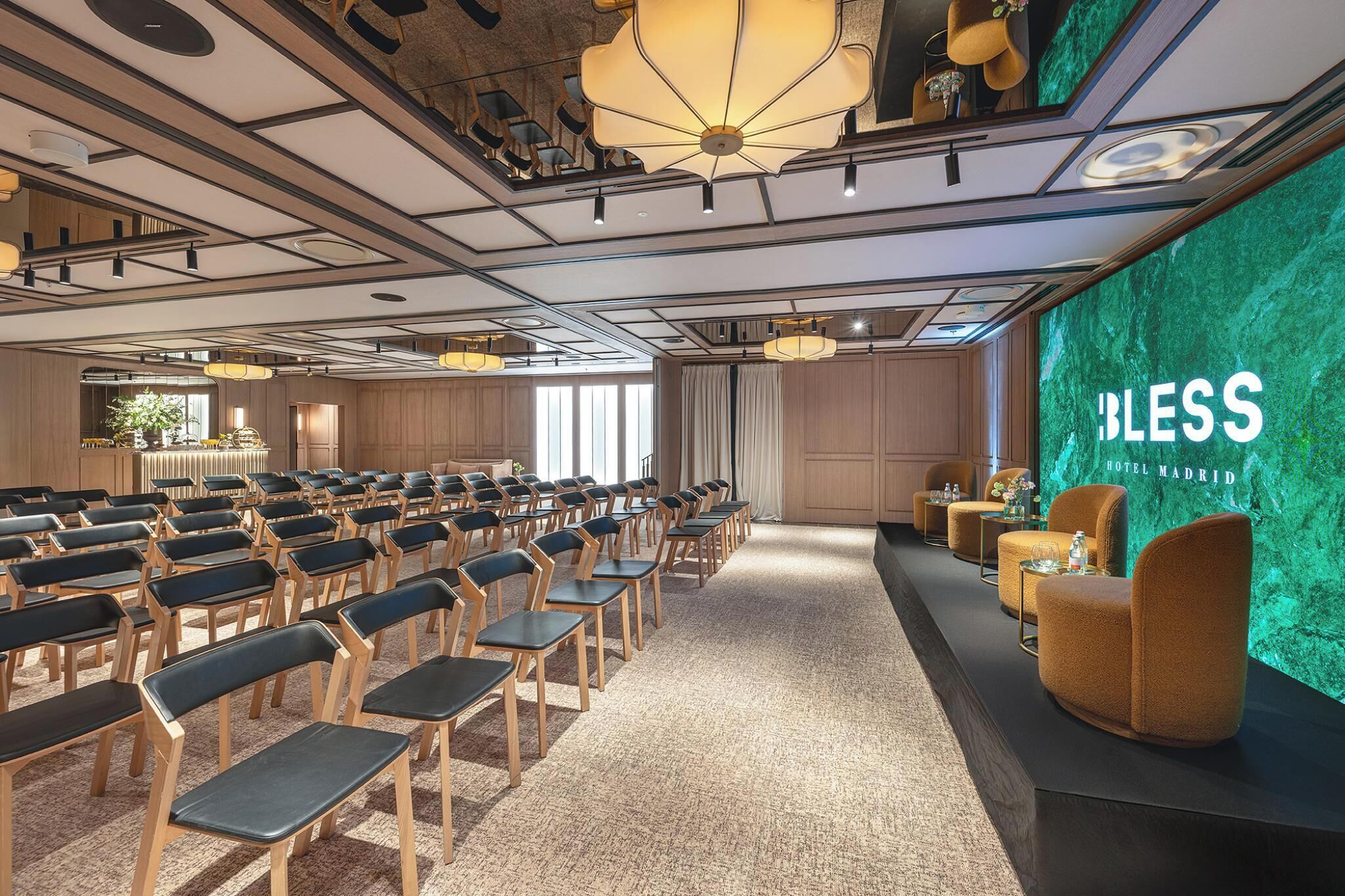 Un salón de conferencias con filas de sillas, un escenario con fondo y una zona de asientos con sofás.